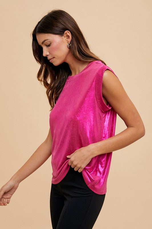Woman wearing a bright pink metallic top and black pants against a beige background.