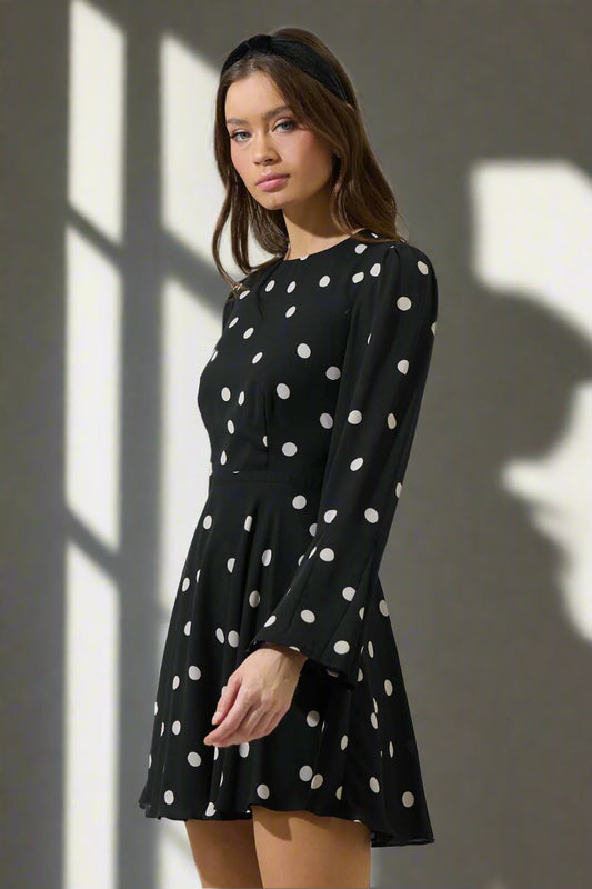 Woman wearing a black dress with white polka dots against a plain background