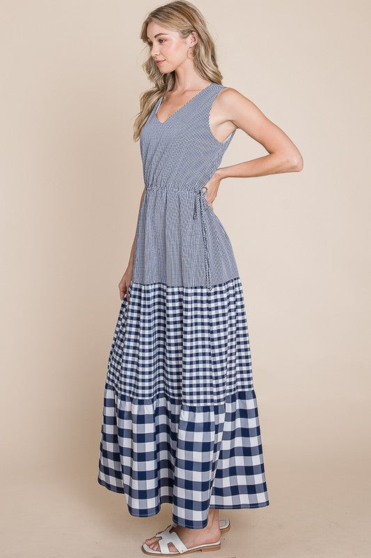 A model wearing a blue and white gingham patterns woven maxi dress with a v-neckline and no sleeves.