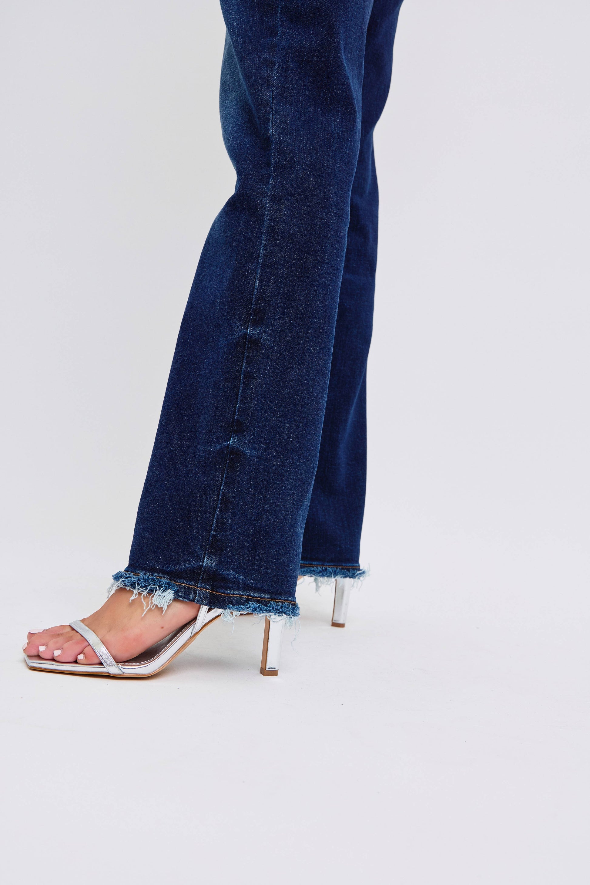Blue jeans with a frayed hem worn with high-heeled sandals on a white background