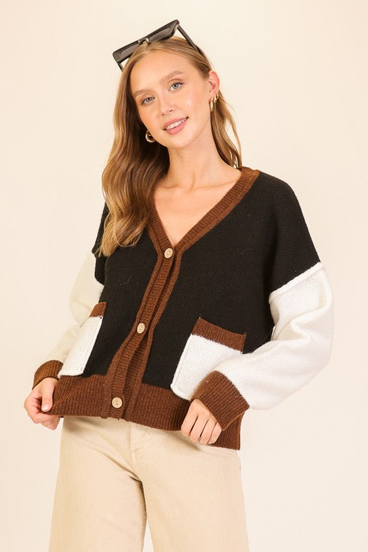 Woman wearing a black, brown, and white color-blocked cardigan on a beige background