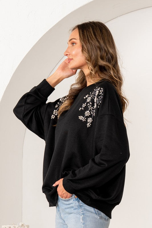 Woman wearing a black sweatshirt with floral embroidery against a white background