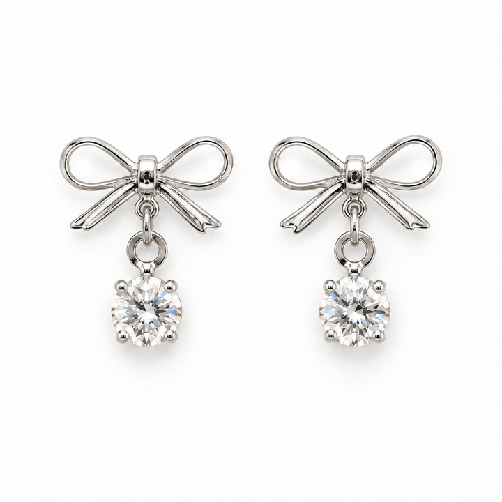 A pair of silver bow stud earrings with clear round-cut gemstones hanging below, shown on a plain white background.