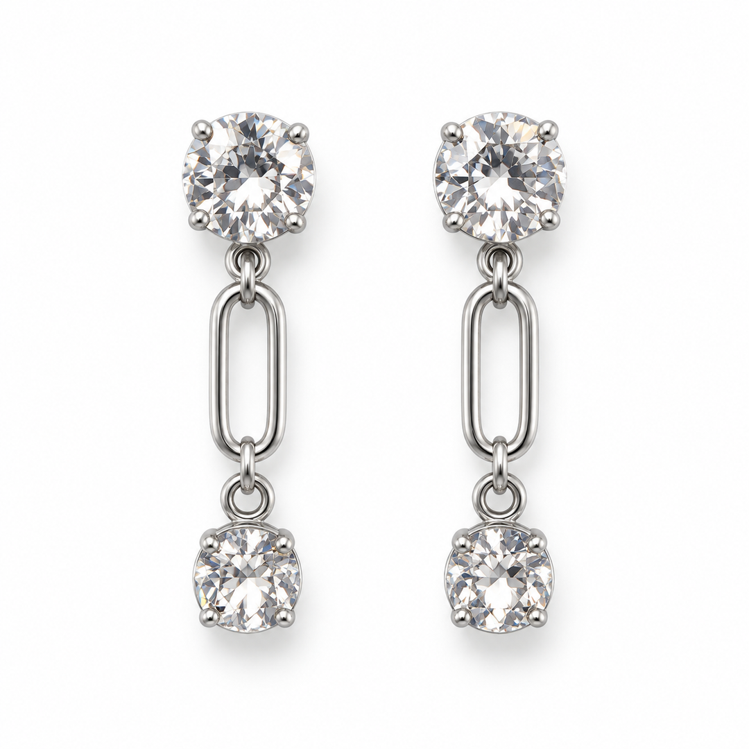 A pair of silver-toned dangle earrings with a large round clear gemstone at the top, an elongated oval link in the middle, and a smaller round clear gemstone at the bottom, shown on a plain white background.