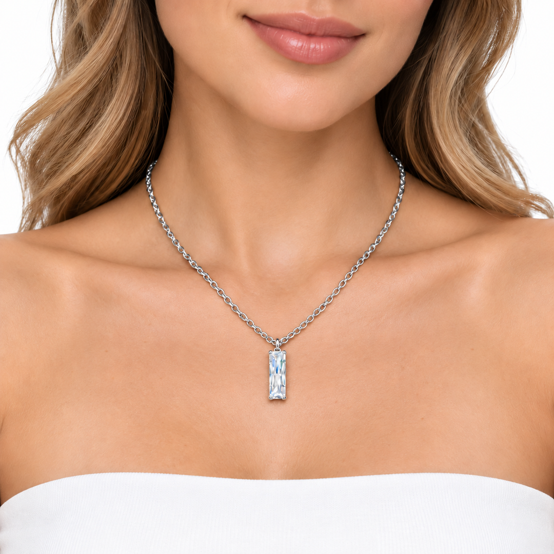 A close-up of a woman wearing a silver-toned chain necklace with a rectangular pendant featuring a textured, iridescent blue and white pattern, set against a clean white background.