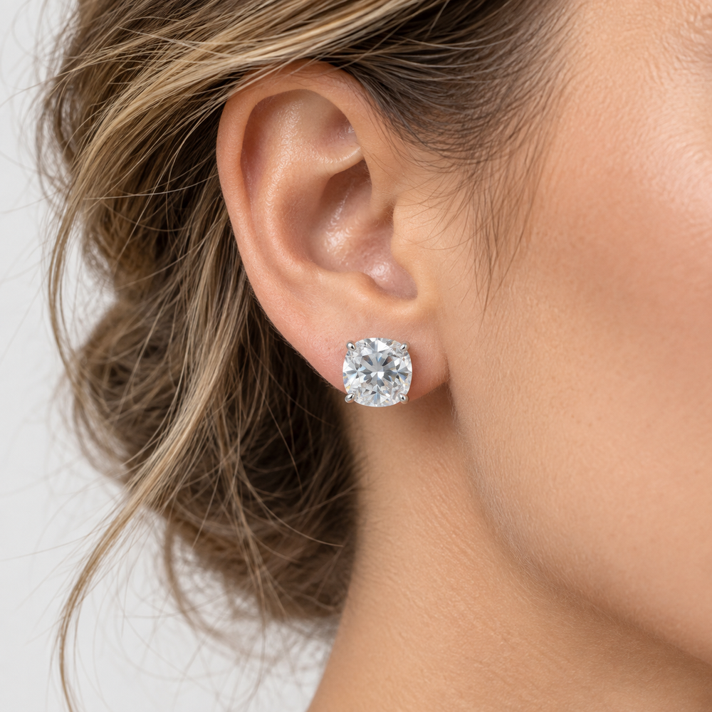 A close-up of a woman's ear wearing a single round brilliant-cut diamond stud earring in a silver-toned setting against a light gray background.