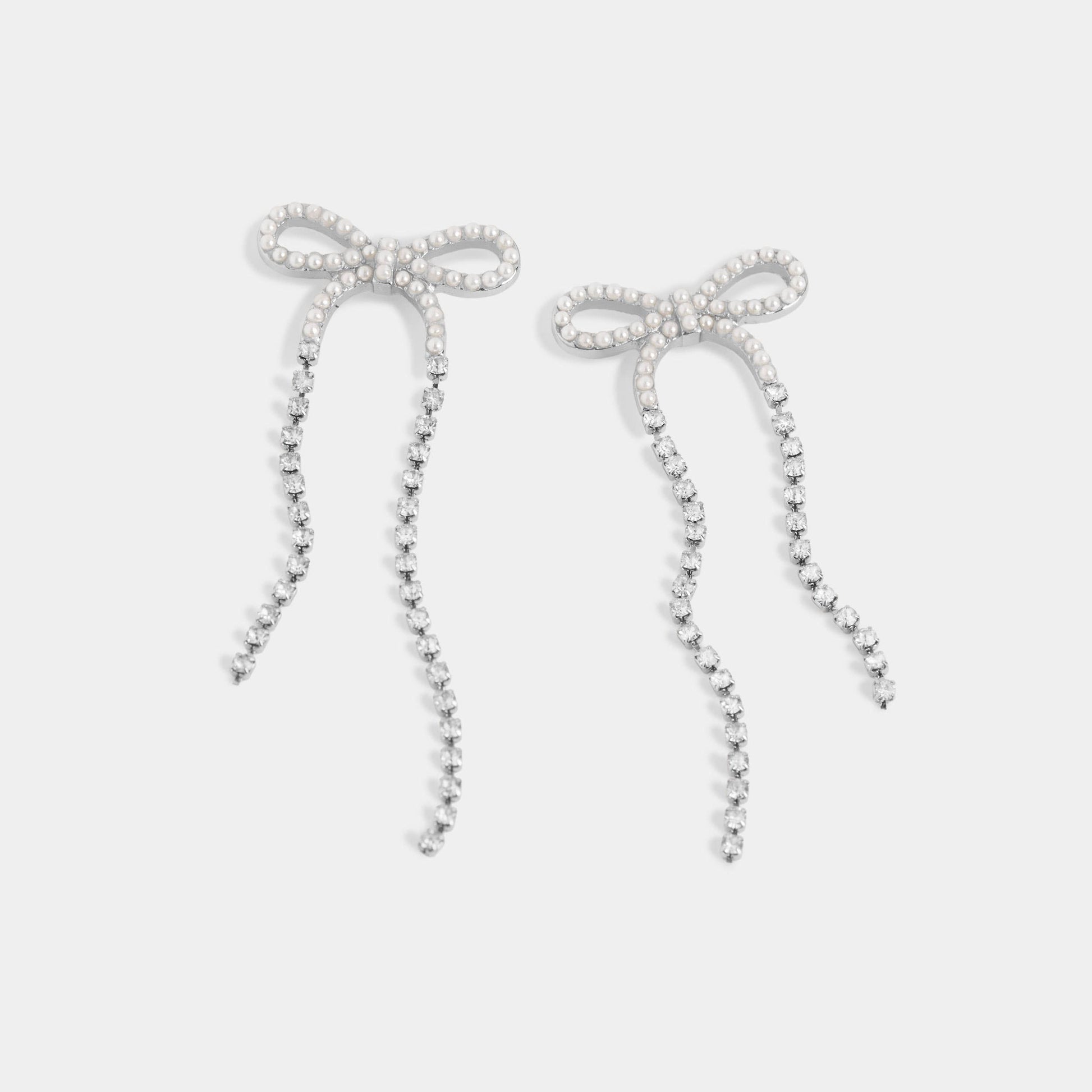 Bow-shaped earrings with pearl details on a light gray background