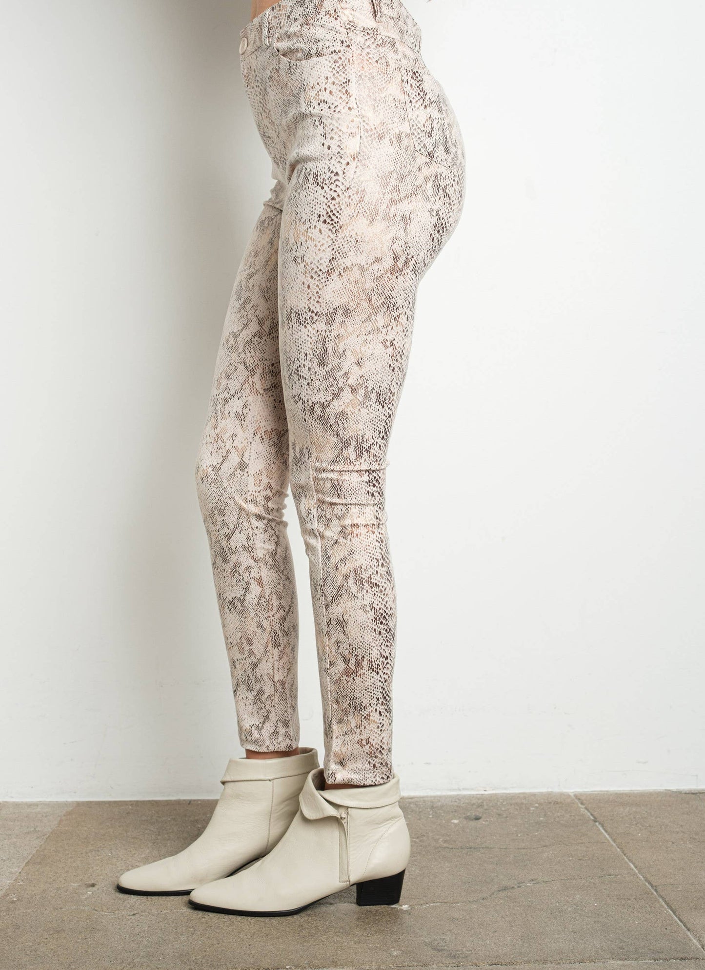 Person wearing beige patterned leggings and white boots on a plain background