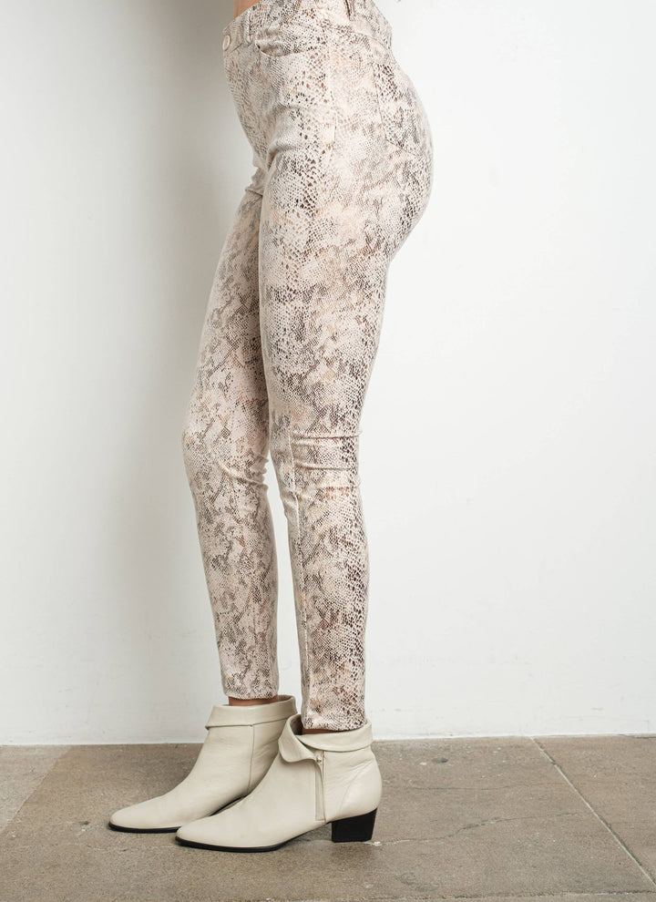 Person wearing beige patterned leggings and white boots on a plain background