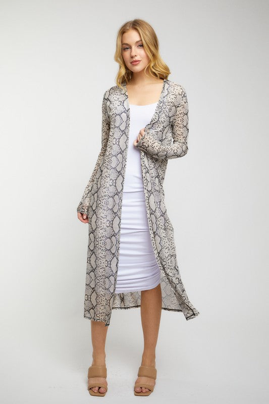 Woman wearing a long snake print coat over a white dress on a plain background