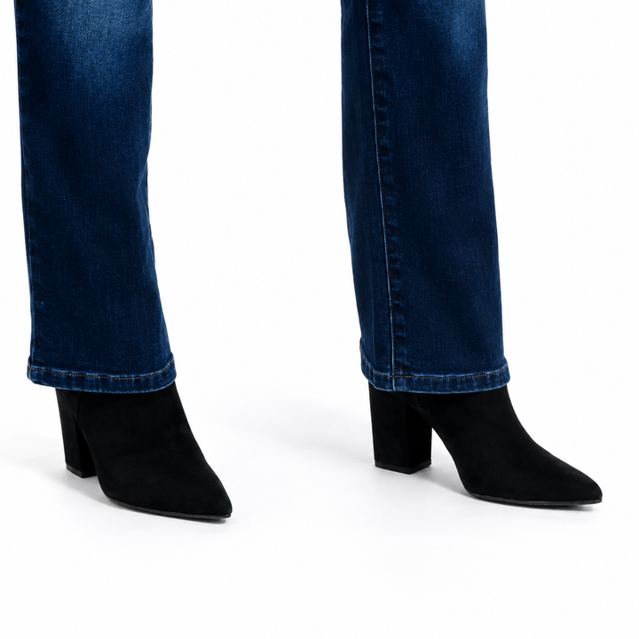 Black pointed-toe ankle boots with block heels, shown on a model wearing dark blue jeans against a white studio background.