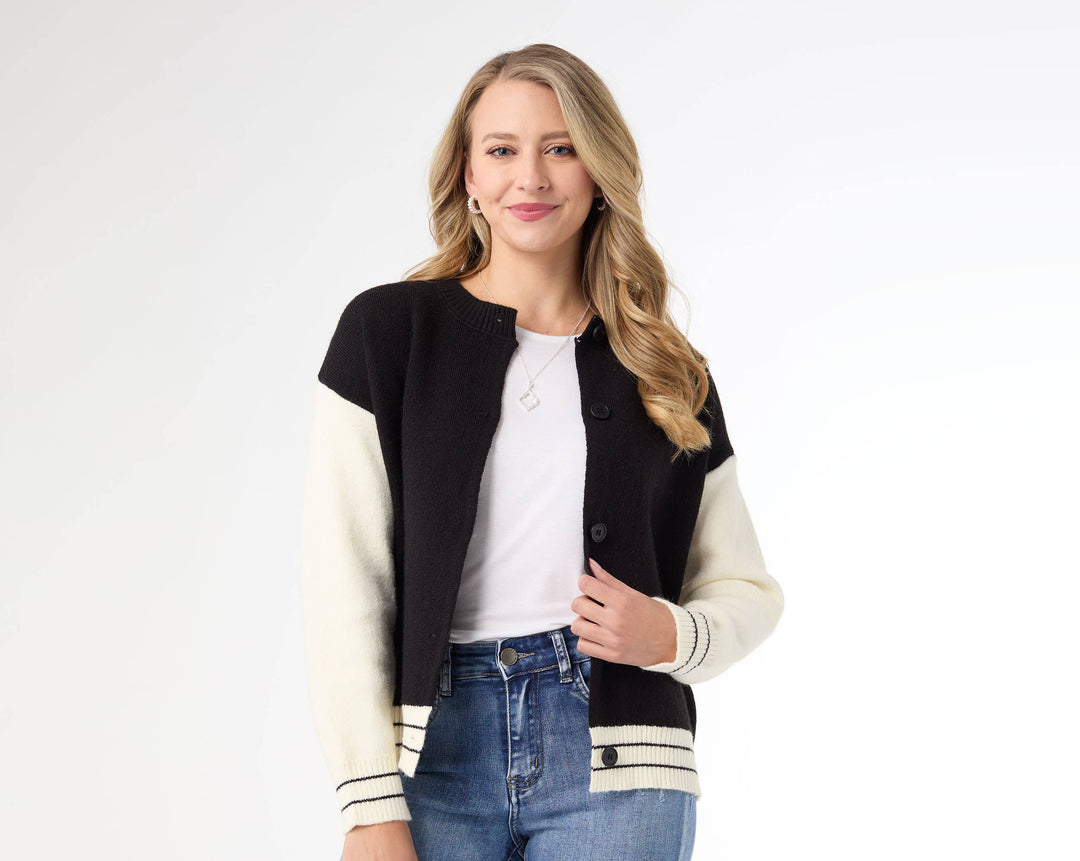 Woman wearing a black and white varsity jacket with blue jeans on a white background