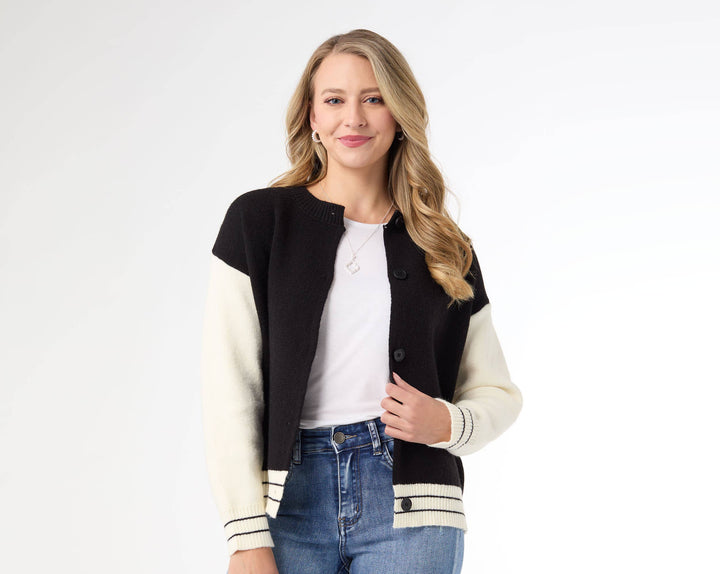 Woman wearing a black and white varsity jacket with blue jeans on a white background
