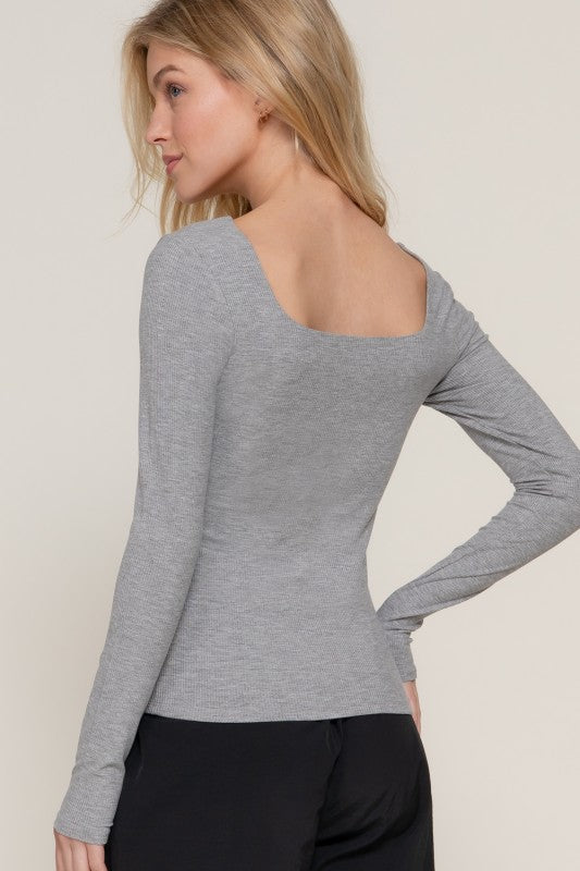 Woman wearing a gray long-sleeve top with an open back against a plain background