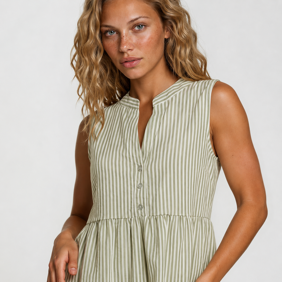A woman wearing a sleeveless, V-neck dress with vertical stripes in sage green and cream, photographed against a light gray studio background.