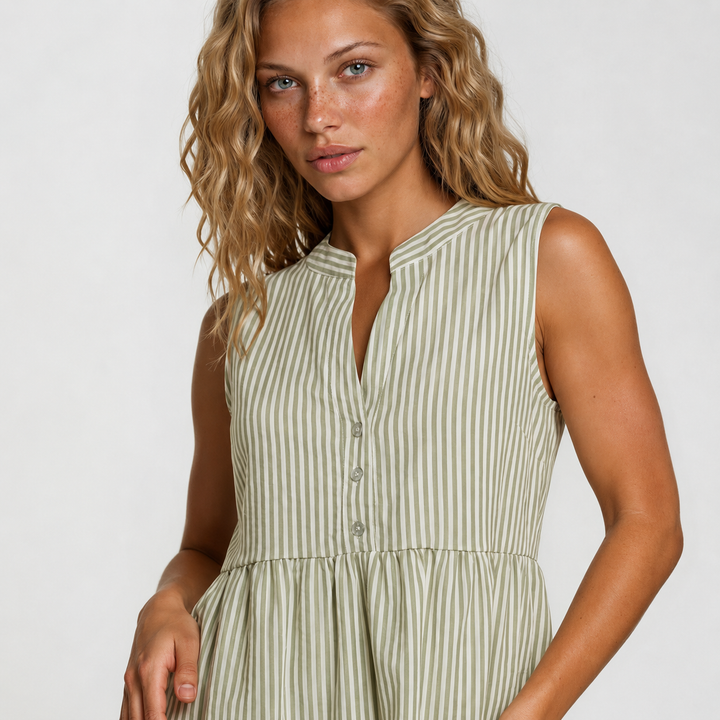 A woman wearing a sleeveless, V-neck dress with vertical stripes in sage green and cream, photographed against a light gray studio background.