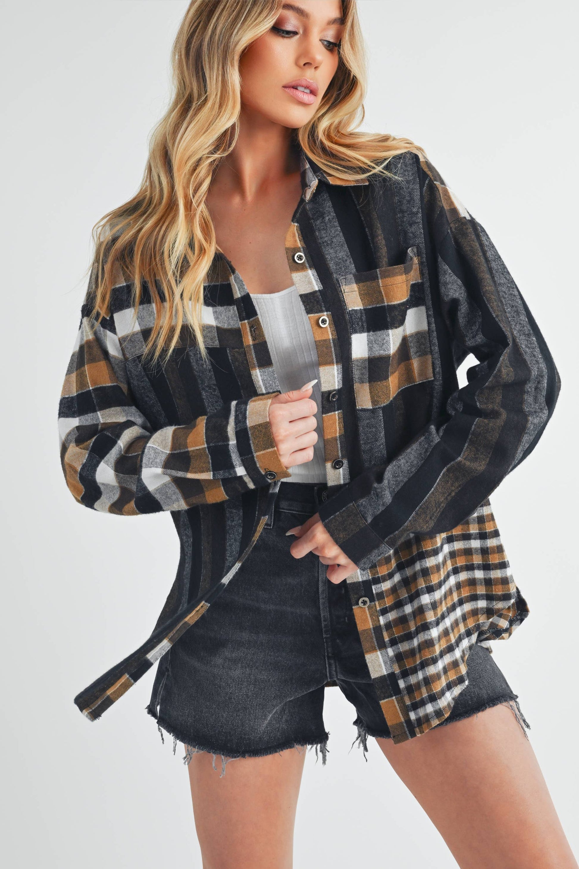 Woman wearing a plaid shirt over a white top and denim shorts on a white background