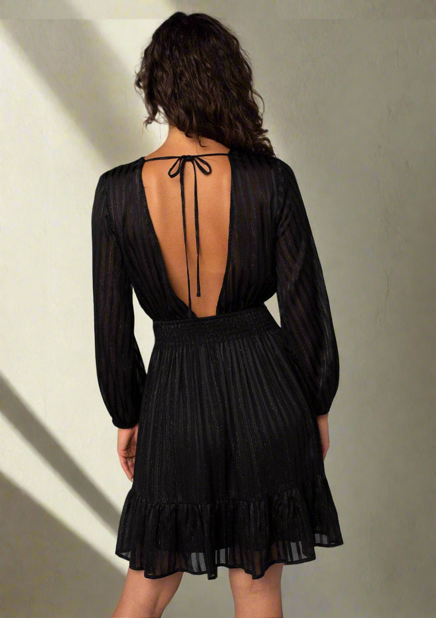 Black dress with sheer long sleeves and open back on a plain background