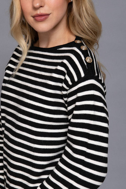 Black and white striped sweater with gold buttons worn by a person against a gray background
