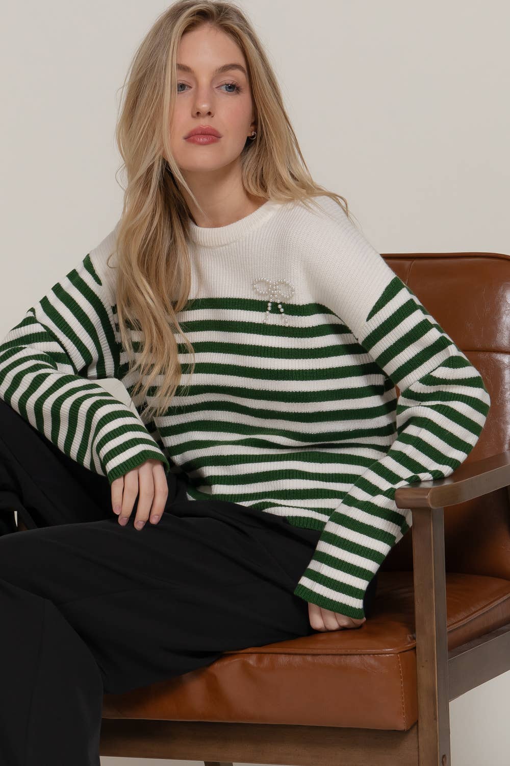 Woman wearing a green and white striped sweater sitting on a brown leather chair.