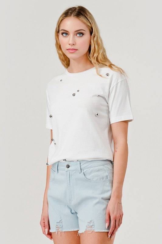 Woman wearing a white t-shirt with button details and light blue denim shorts on a plain background