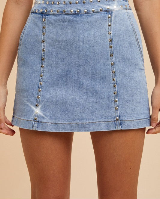 Light blue denim skirt with studded details on a beige background
