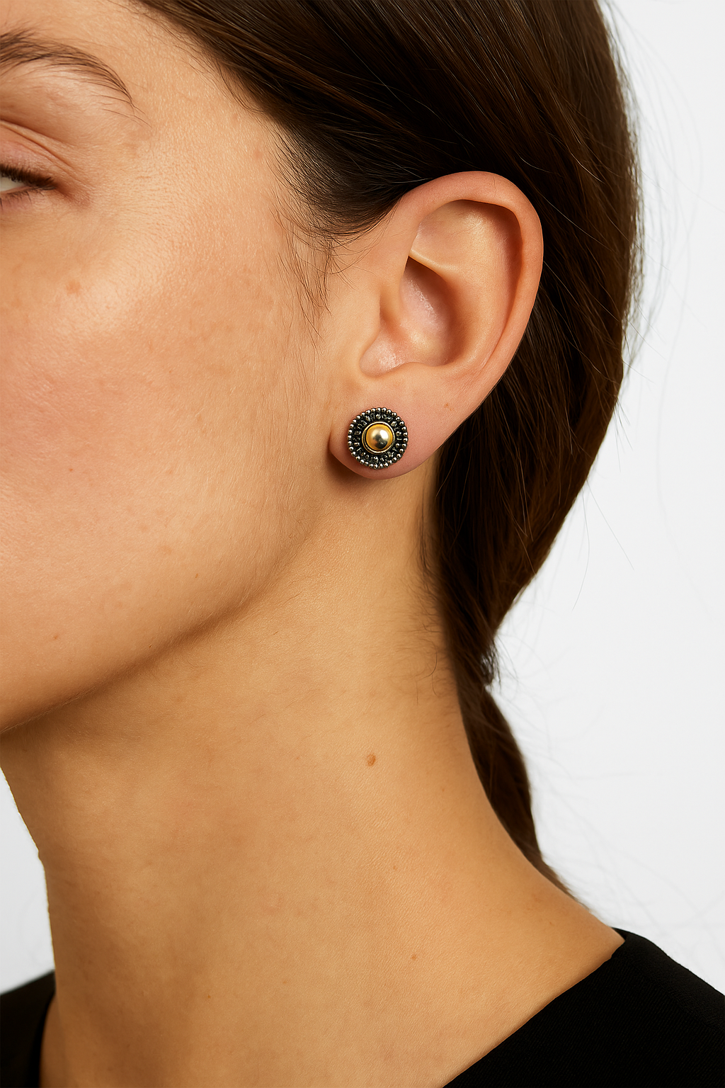 Close-up of a person wearing a gold and black earring on a plain background
