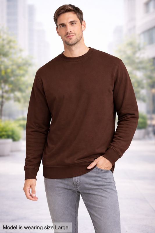 Man wearing a brown sweatshirt and light gray jeans standing outdoors.