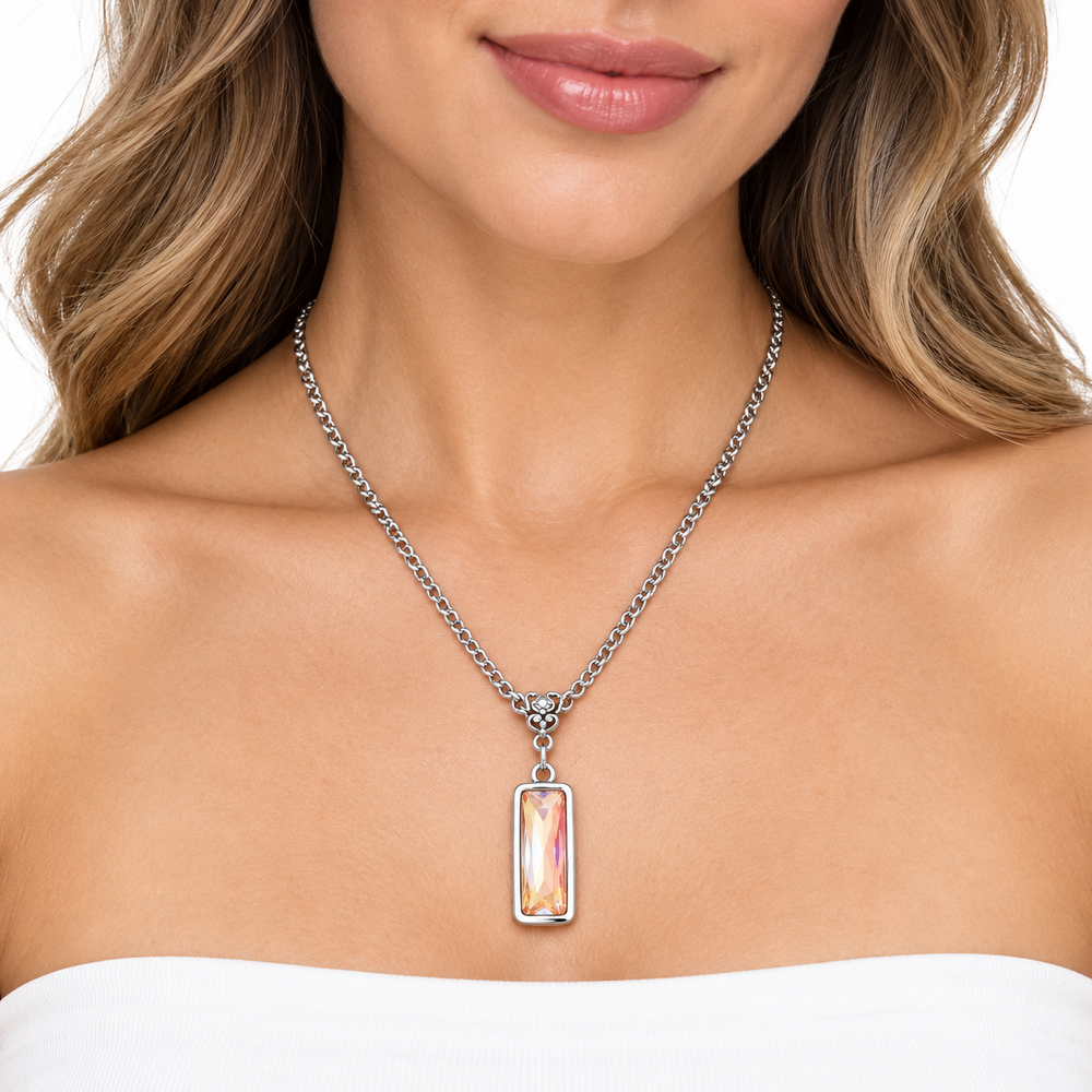 A close-up of a woman wearing a silver chain necklace with a rectangular pendant featuring an iridescent, rainbow-like inlay.