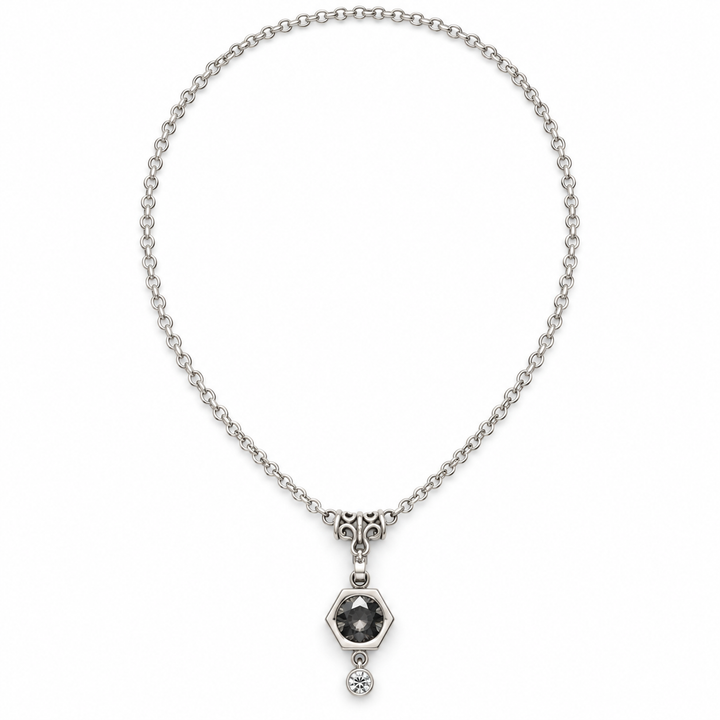 A silver chain necklace with a central hexagonal pendant featuring a dark gray round stone and a small dangling clear crystal, shown on a plain white background.