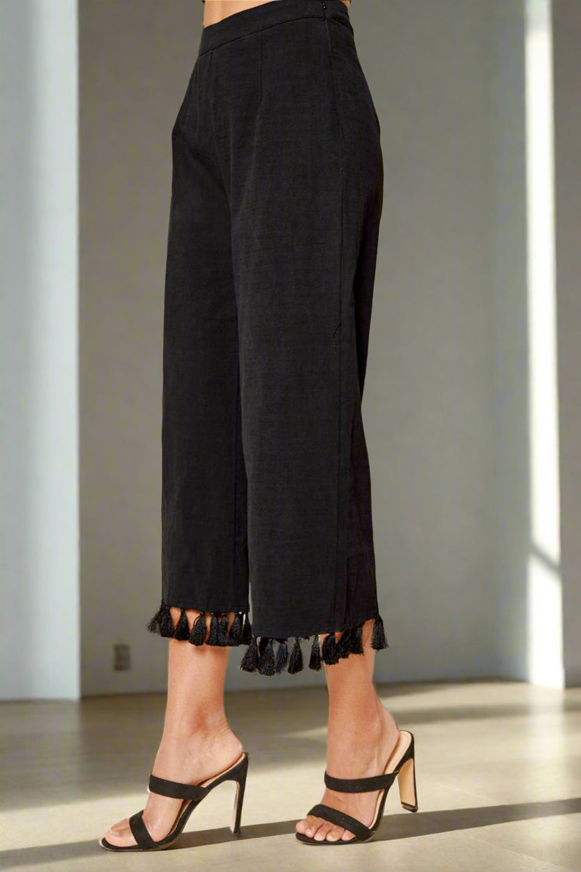 Black wide-leg pants with tassel details worn by a person on a beige background