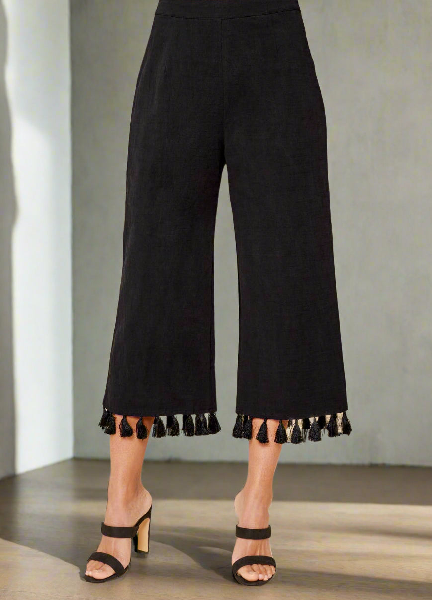 Black tasseled pants worn by a person on a beige background