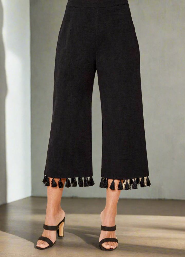 Black tasseled pants worn by a person on a beige background