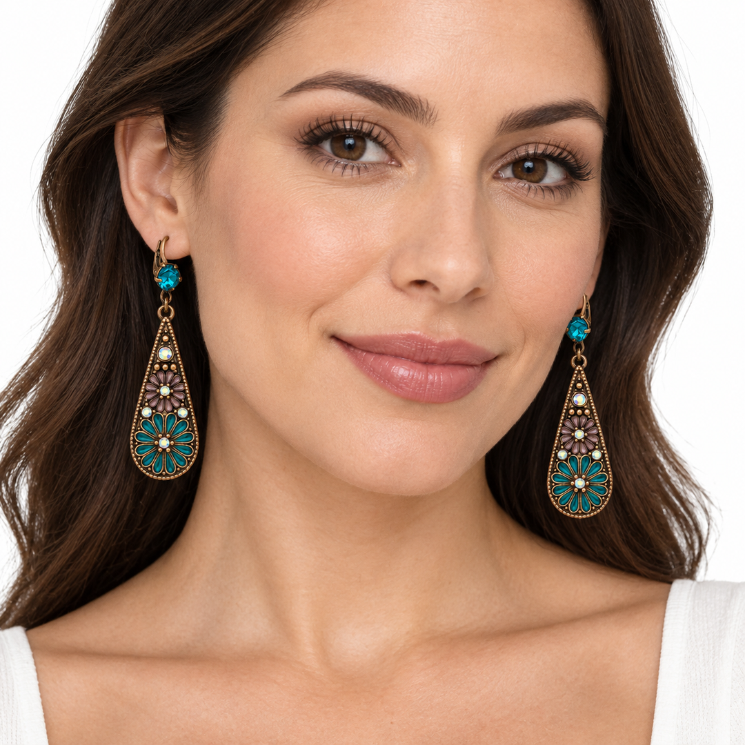 A close-up of a woman wearing ornate gold-tone dangle earrings with turquoise blue and white floral details, set against a clean white background.