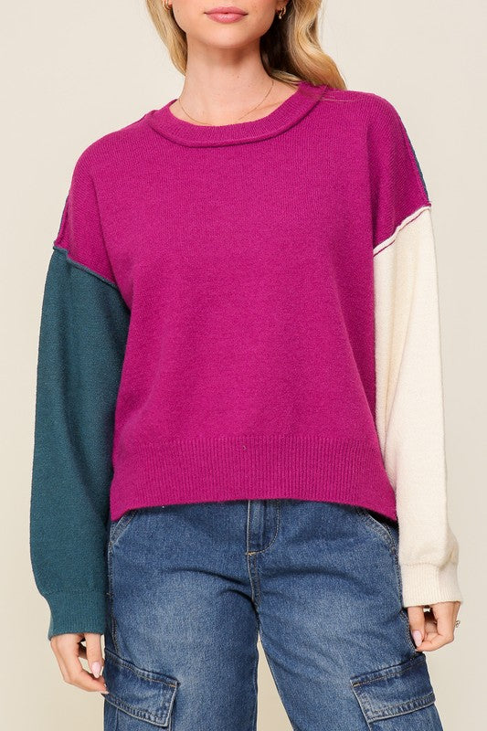 Person wearing a colorful sweater with magenta, teal, and beige sleeves on a plain background
