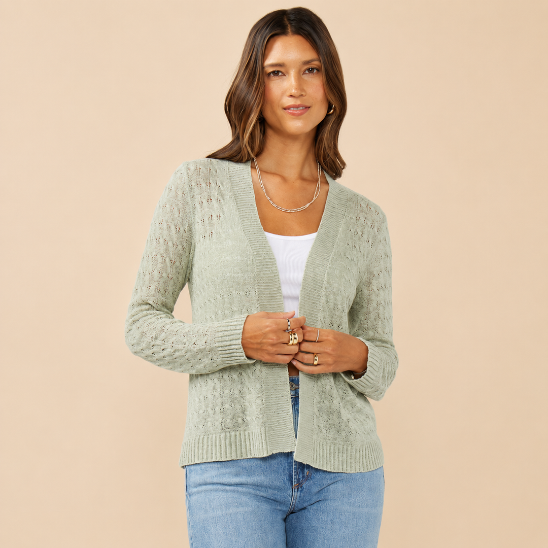 Woman wearing a light green cardigan over a white top and blue jeans on a beige background