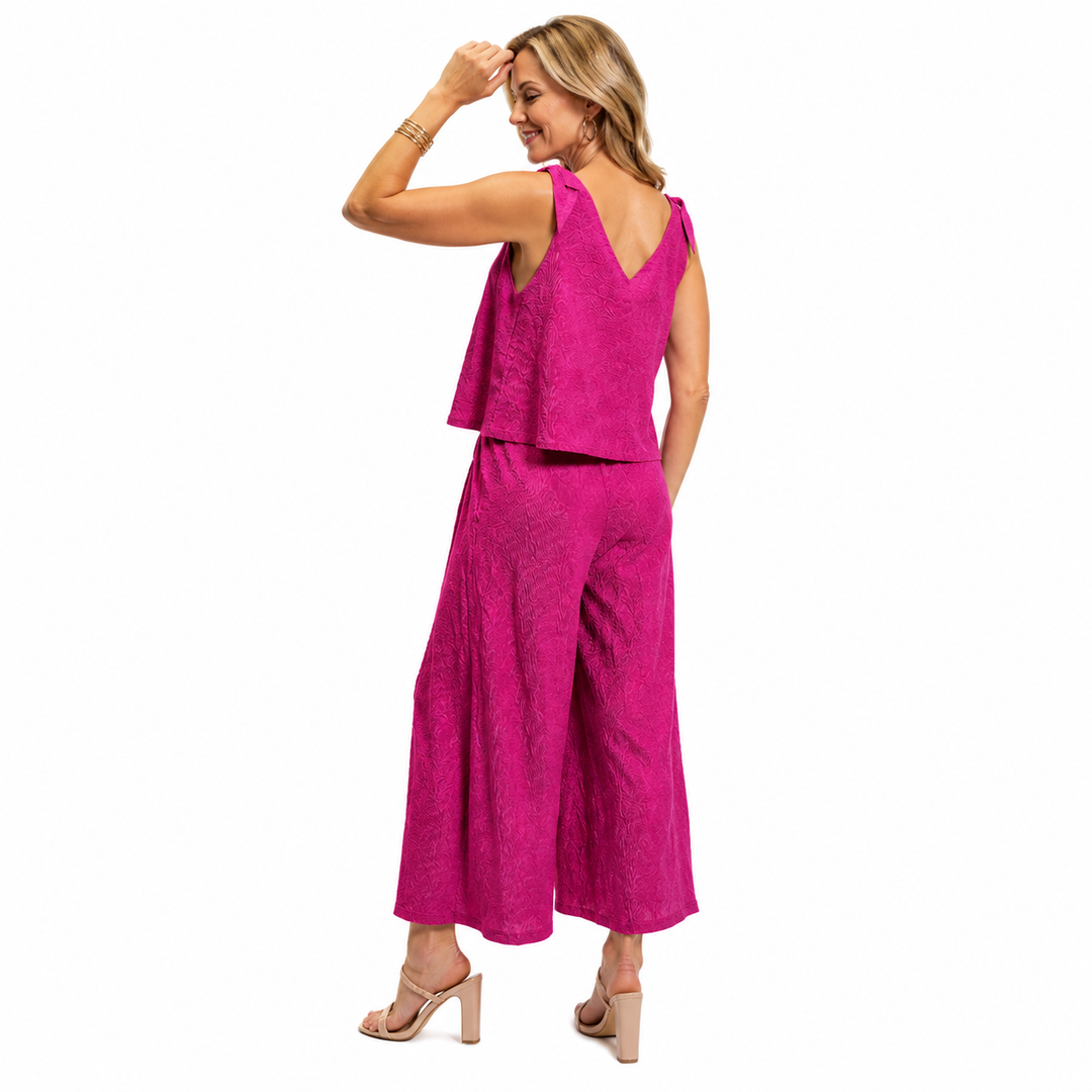 A woman modeling a bright fuchsia crinkle jumpsuit, shown from the back against a plain white background.