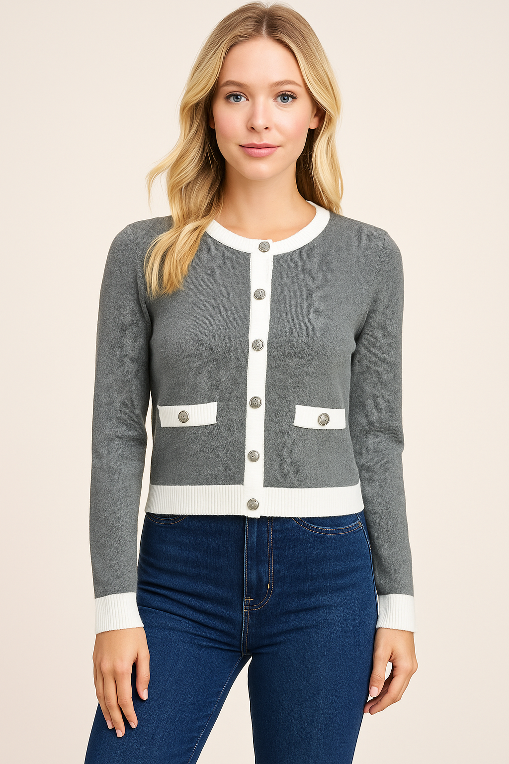 Woman wearing a gray cardigan with white buttons and trim, standing against a beige background.