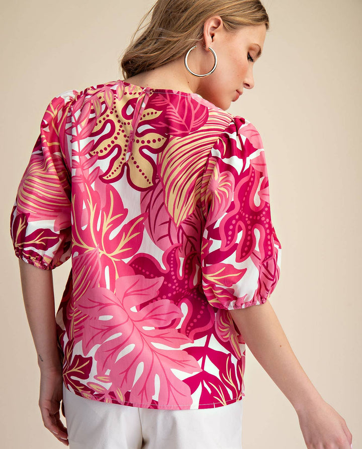 Woman wearing a pink floral blouse and white shorts on a beige background