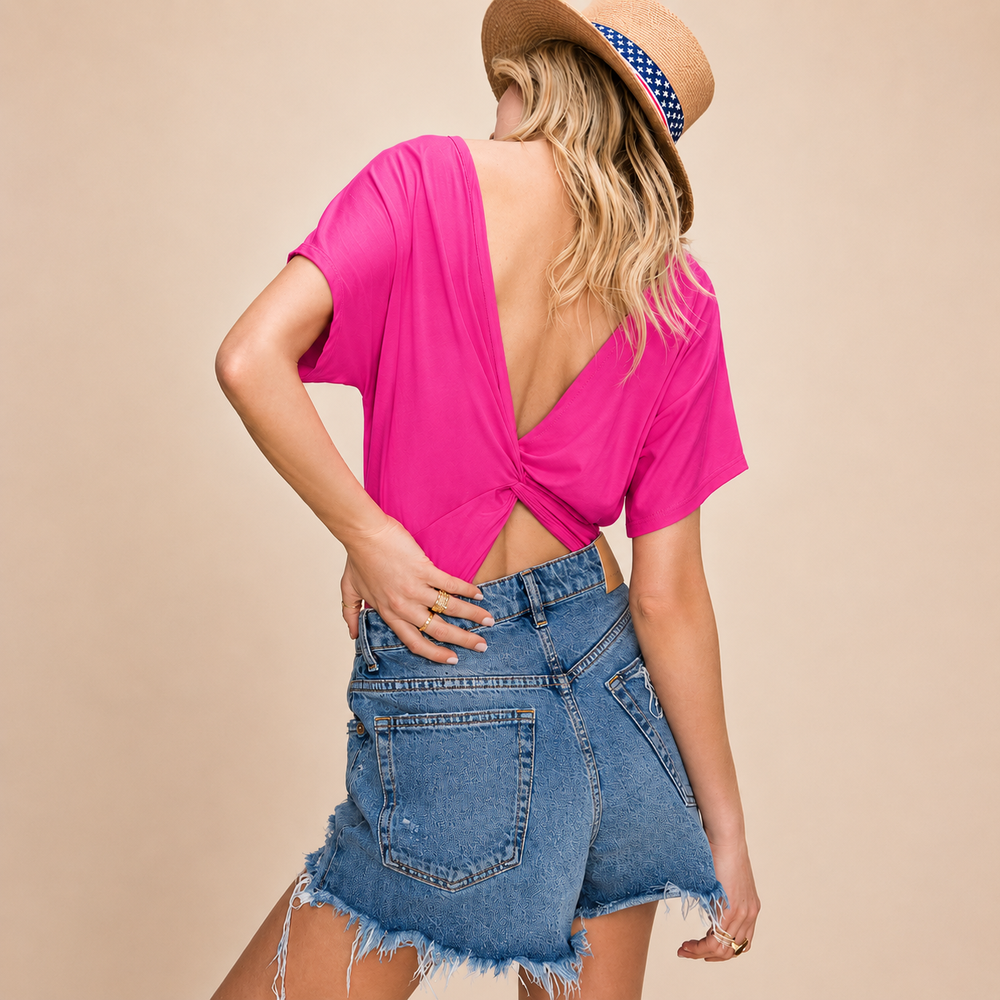 Woman wearing a bright pink top bodysuit and denim shorts with a beige background