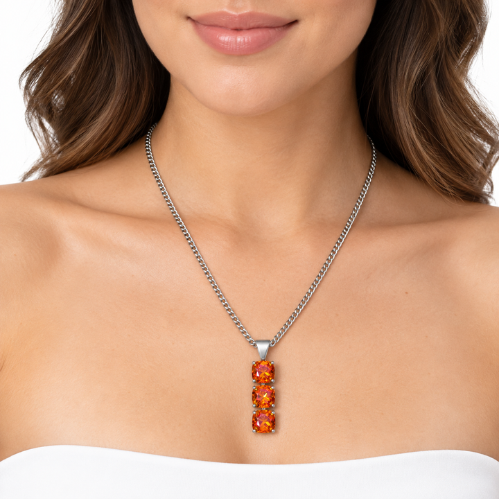 A close-up of a woman wearing a silver chain necklace with a vertical pendant featuring three stacked rectangular orange gemstones.