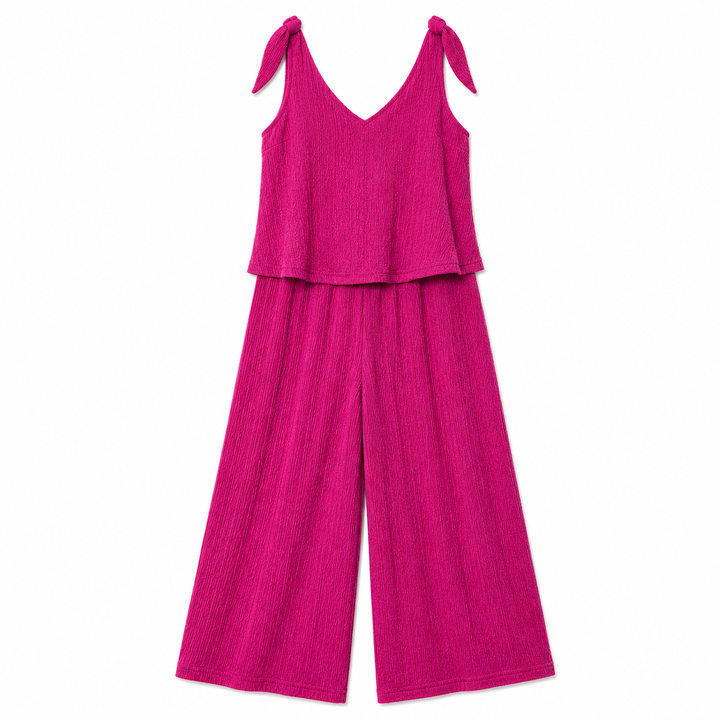 A bright magenta pink sleeveless V-neck jumpsuit with tie shoulder straps made of a textured crinkle fabric, shown on a plain white background.
