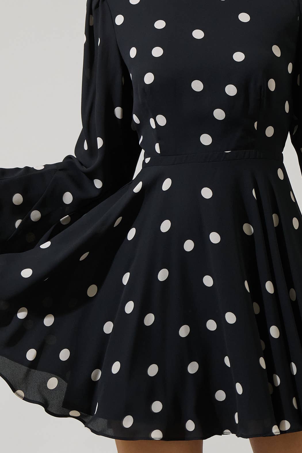 Black dress with white polka dots on a plain background