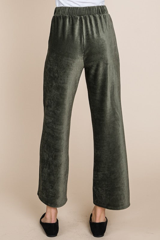 Green velvet pants worn by a person on a beige background