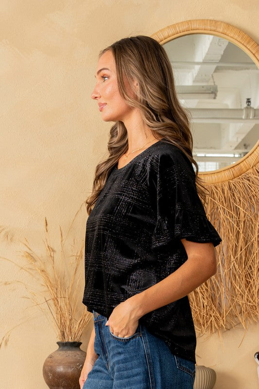 Woman wearing a black textured top and blue jeans standing in front of a mirror.