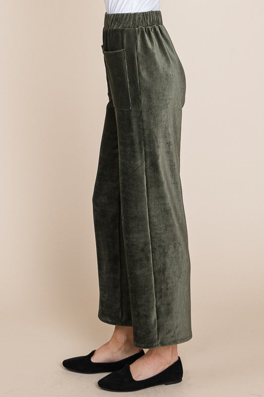 Green velvet wide-leg pants worn by a person on a beige background