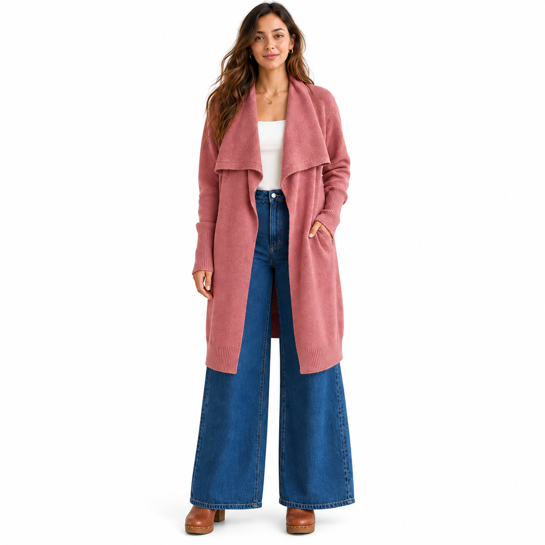A woman modeling a long, dusty pink open-front cardigan over a white top and blue wide-leg jeans, standing against a plain white studio background.
