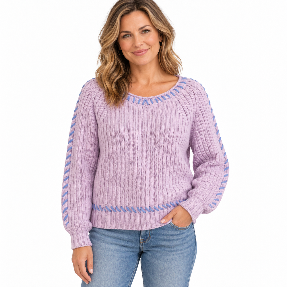 A woman wearing a lavender ribbed knit sweater with blue patterned trim along the neckline, cuffs, and hem, paired with blue jeans, against a plain white background.