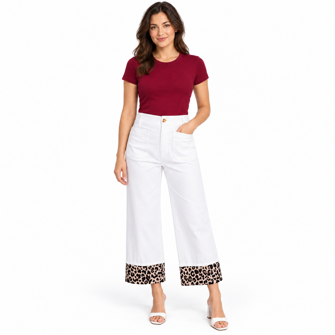 A woman modeling white cropped wide-leg pants with leopard-print turned-up cuffs, paired with a burgundy short-sleeve top and white heeled sandals, against a plain white background.