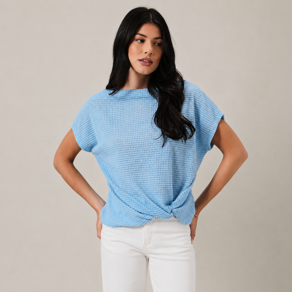 Woman wearing a light blue textured top with white pants on a beige background